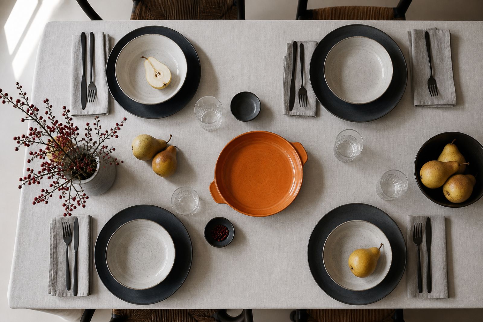 Overhead table setting with circular charcoal plates, pale bowls, pears and one orange serving dish